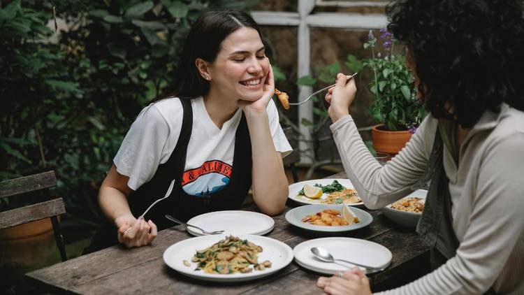 A person feeding another person with fried seafood in garden