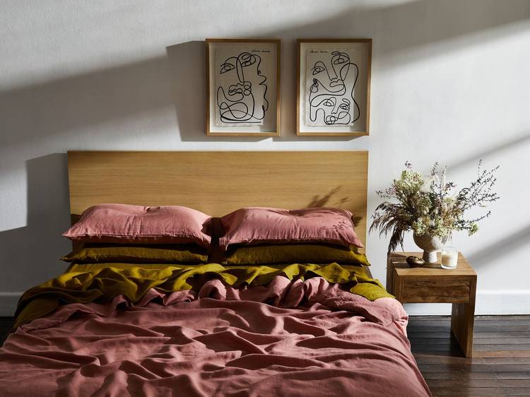 A ruffled bed in khaki and pink linen sheets in a sunny bedroom.