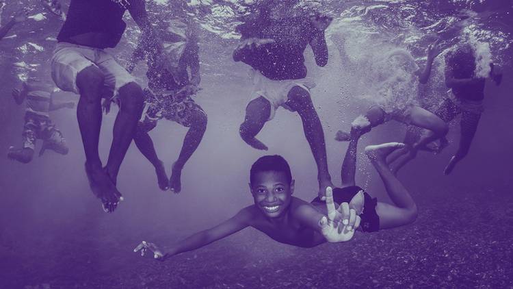 Young refugee boys play underwater. The image has a purple filter