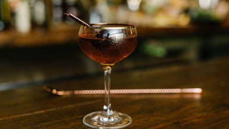 A bourbon cocktail in a fancy glass with a swizzle stick