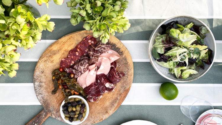 a charcuterie board and green salad on a table with foliage