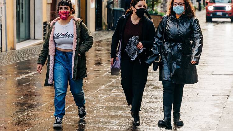 Three women wearing face masks walking down a street after it's rained