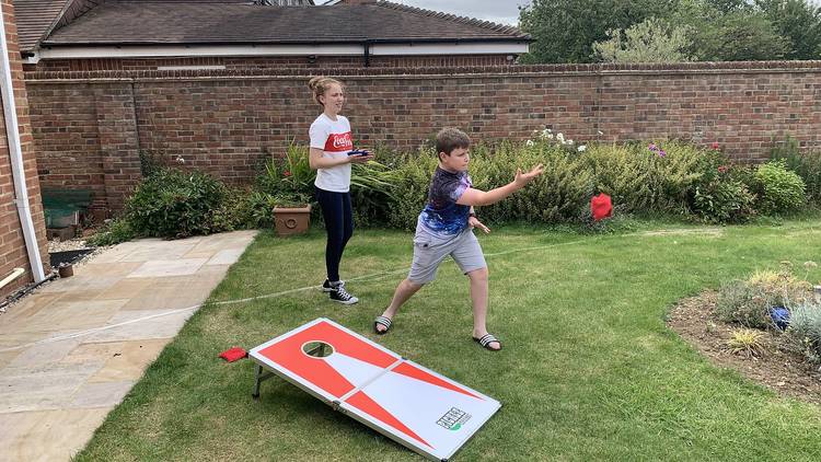 Two children playing a game of cornhole in their backyard.
