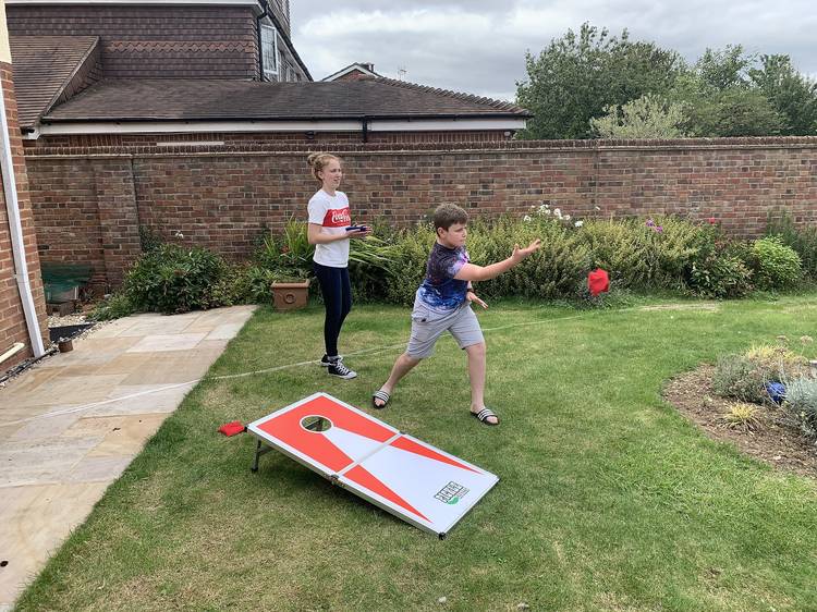 Two children playing a game of cornhole in their backyard.