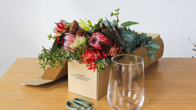 A box of native flowers, a pair of scissors and a glass on a table.