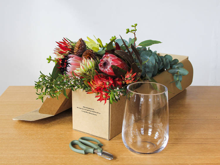 A box of native flowers, a pair of scissors and a glass on a table.