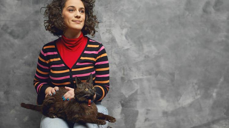 Comedian Jude Perl ini a stripe cardigan holding what looks like a stuffed cat