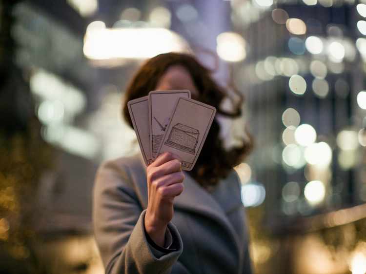 A woman holding three tarot cards to conceal her face.