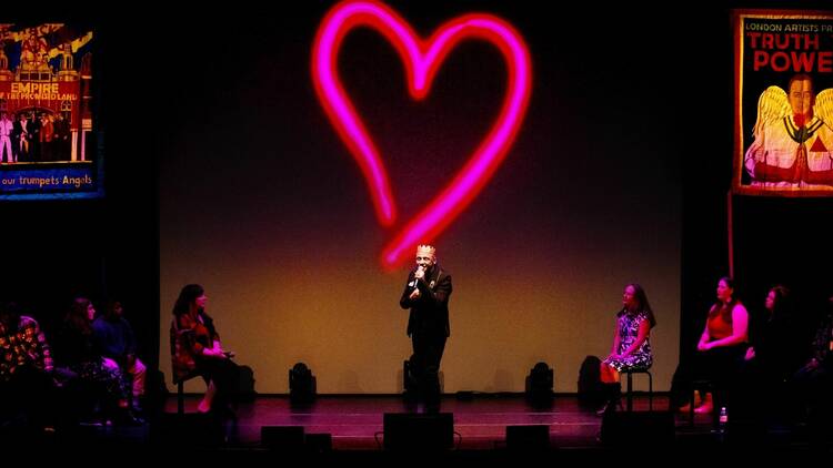 A man performing on stage with a huge neon heart in pink on the backdrop behind him