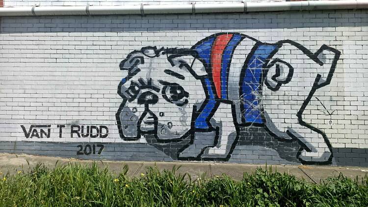 A mural of a white, cartoon-style bulldog. The dog is cocking its leg and wearing a Western Bulldogs jersey
