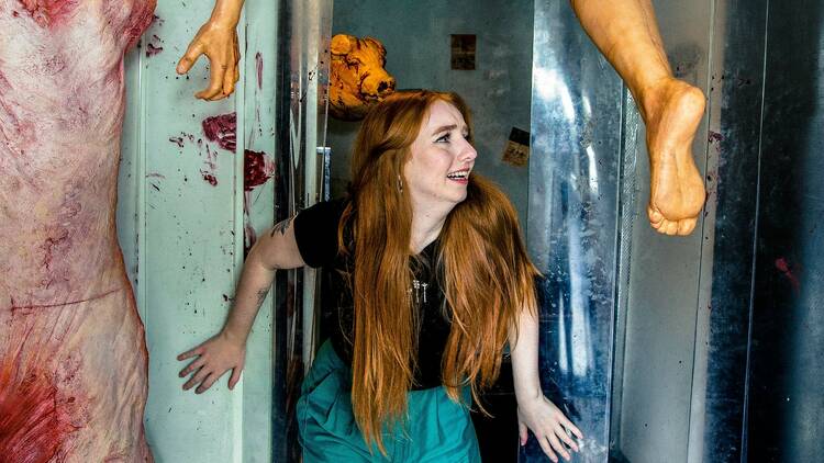 A ginger woman looking scared in a room decorated to look like an abbatoir