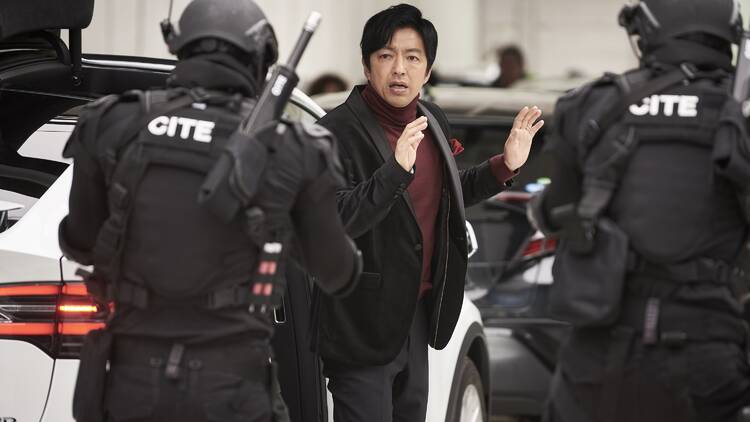 A man in a black suit and maroon t shirt is surrounded by riot police