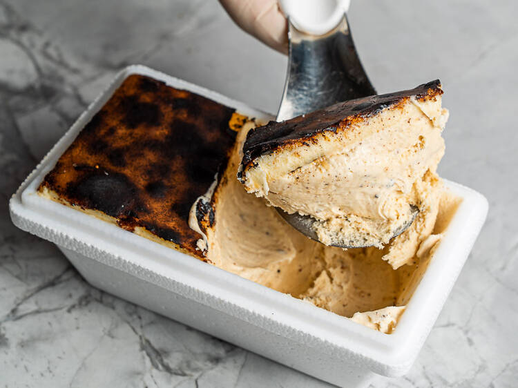 A scoop of Basque cheesecake gelato is being taken from a polystyrene tub on a white and grey marble counter