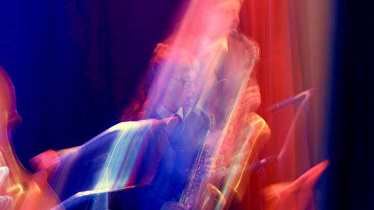 Musician Flora carbon playing the saxophone with a funky pink and blue filter on the image