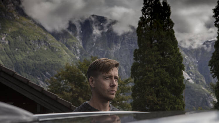 A man exits a car into a cold, mountainous landscape