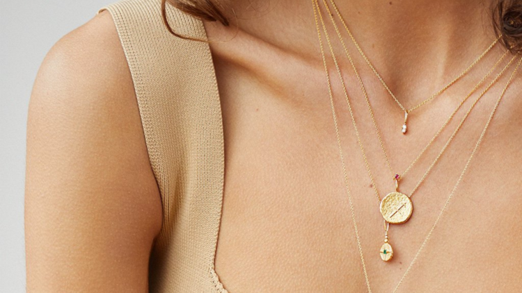 A woman wearing a gold zodiac necklace featuring the Gemini symbol. 