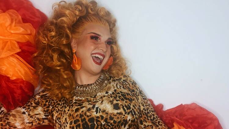 Drag queen Aurora Arsenic smiles and strikes a pose while wearing a leopard print onesie