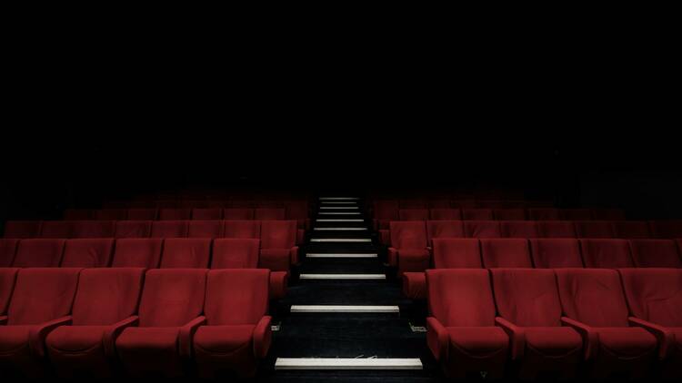 An empty cinema with rows of red chairs and a walkway through the middle