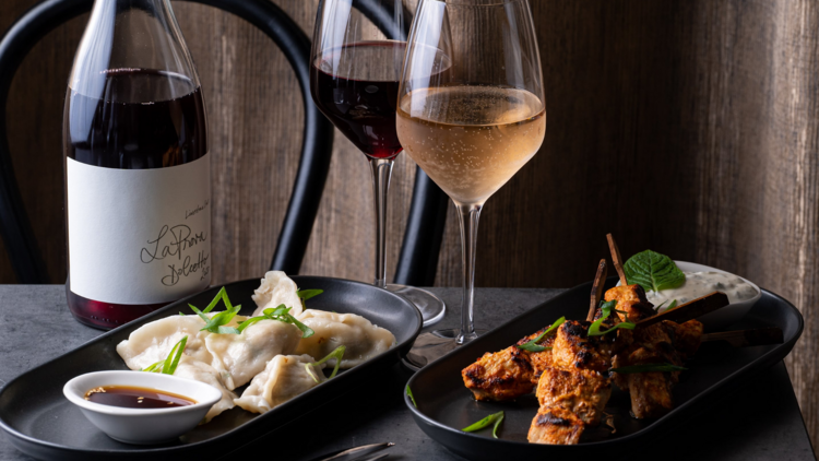A slate table with a plate of dumplings and a glass of rose, a glass of red wine