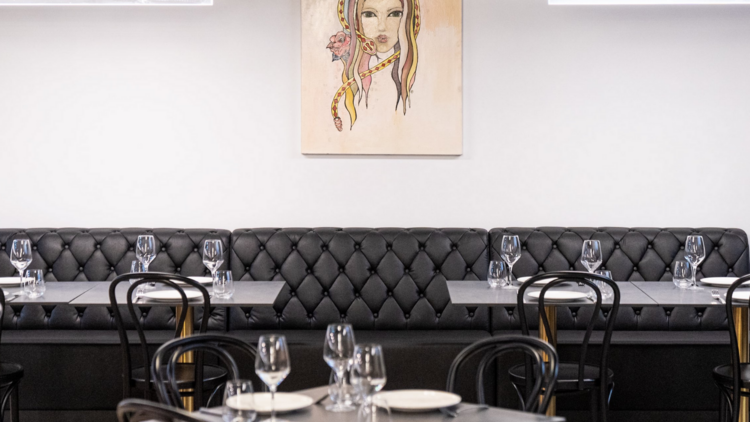 A black leather banquet seat and a white wall with portrait of a woman