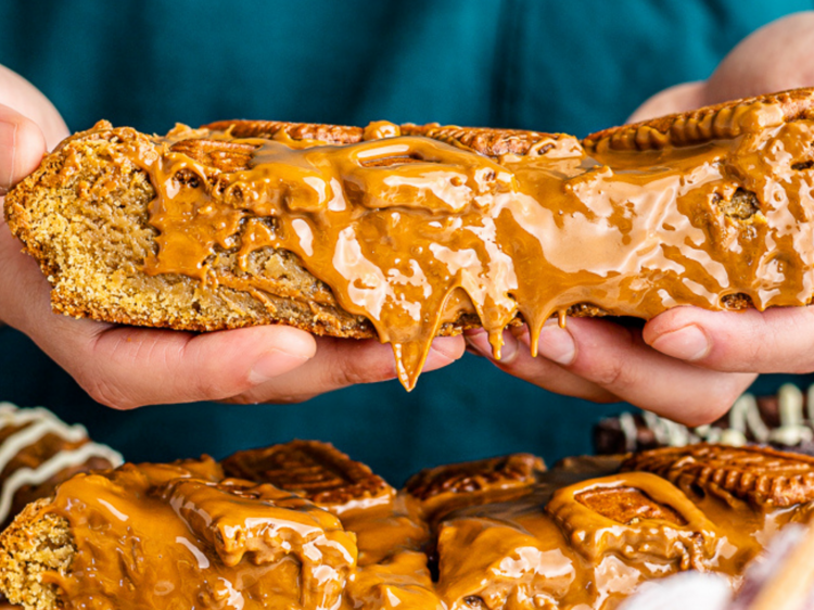 A person is holding up a large cookie which has been sliced in half and is oozing Biscoff caramelised spread