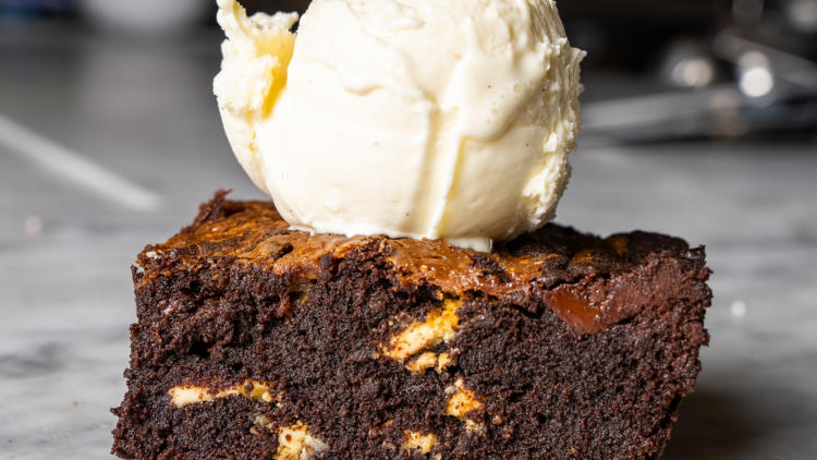 A chocolate brownie on a marble counter with a scoop of icecream on top