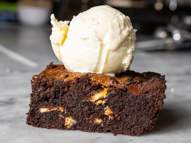 A chocolate brownie on a marble counter with a scoop of icecream on top