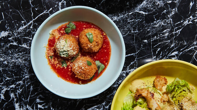 The arancini and caesar salad at Sestina in Culver City against a black and white marble backdrop.