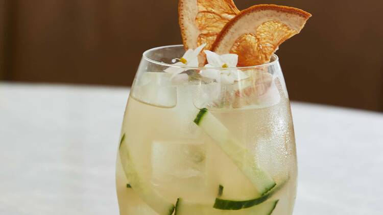 A cocktail with cucumber and orange garnish in a rounded glass