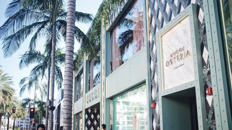 The exterior of Gucci Osteria on Rodeo Drive with palm trees and passerby outside.