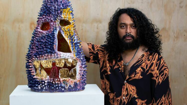 exciting contemporary artist Ramesh Mario Nithiyendran posing with a crystal like purple sculpture one of his cool sculptures of ritualistic icons designed to protect from evil 