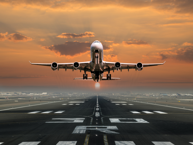 A plane takes off from a runway against an orange sky