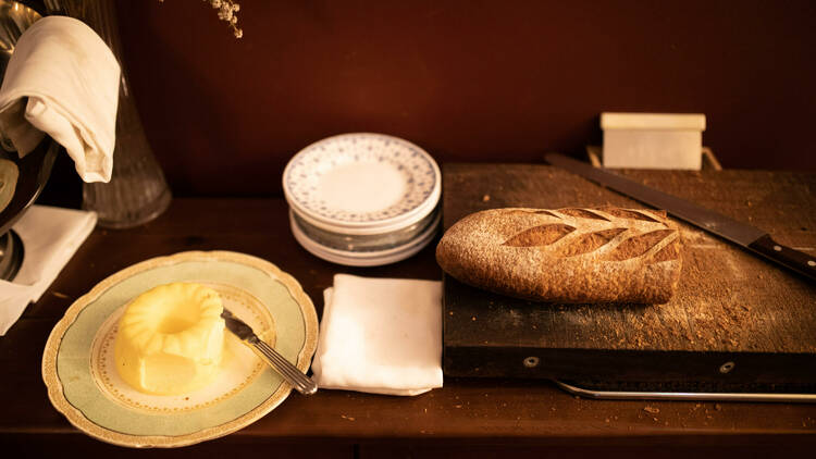 A crusty baguette and butter sit on a wooden counter at Porcine