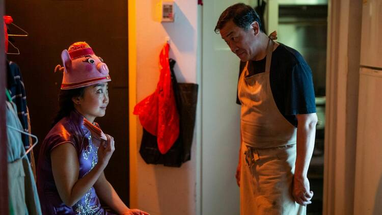 a woman in a lace drace with a pink wooly hat on sitting in  wardrobe with an older man in a butcher's apron looking at her