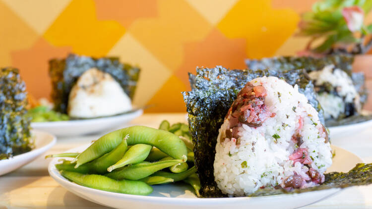 Four rice balls, with one in focus, made with pickled umeboshi plums and a side of edamame.