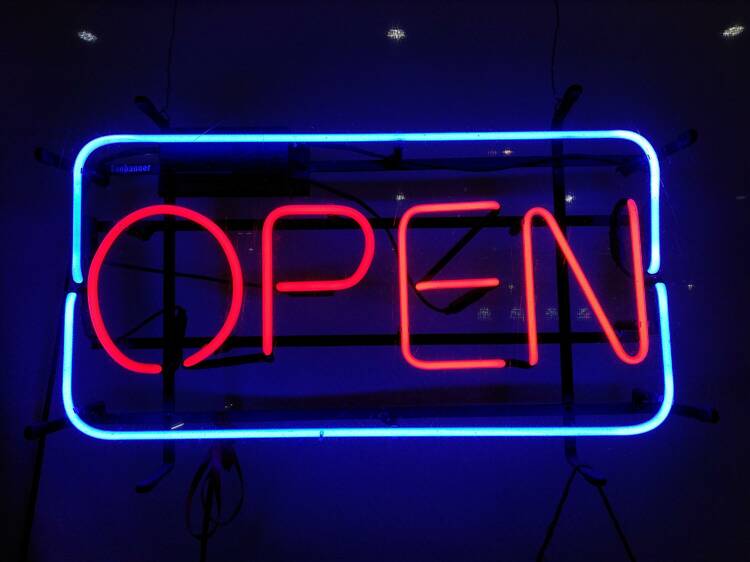 A neon sign made up of a blue box with the word OPEN in red letters sits on a dark background