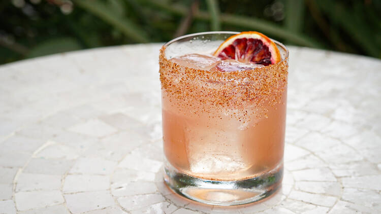 The Death Valley Daisy cocktail at Esters Wine Shop and Bar in Santa Monica. It is pale pink and has a salt rim with a blood orange citrus garnish.