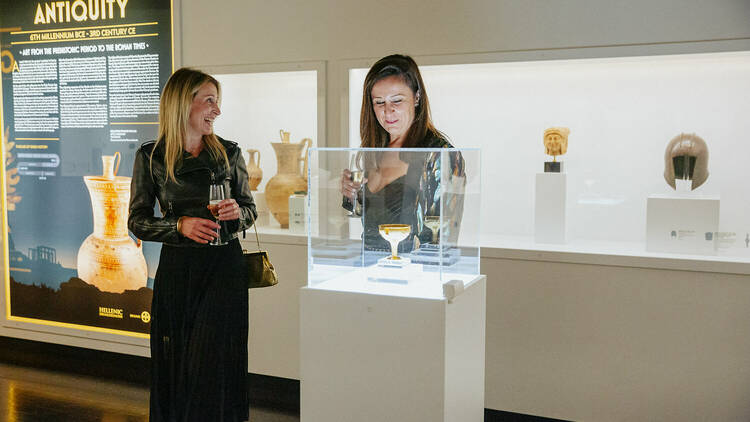Two women looking a golden goblet behind a Perspex box on a plinth