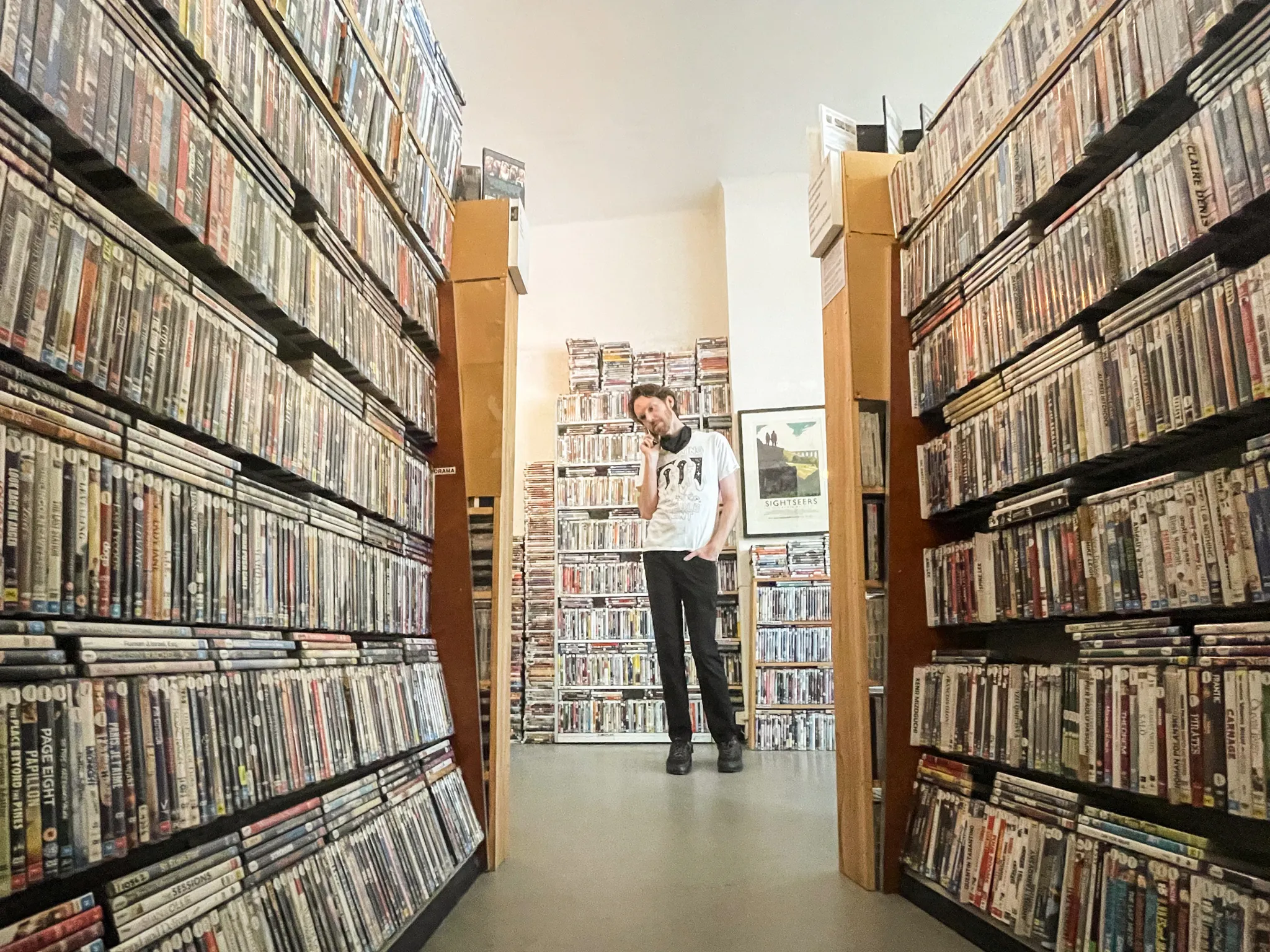 Film Club owner Ben Kenny stands at the end of aisles packed wall to wall with DVD cases.