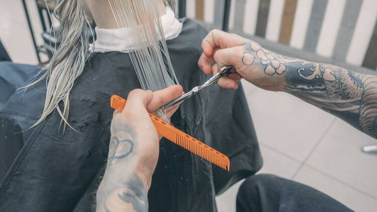 A pair of tattooed hands giving someone a haircut.