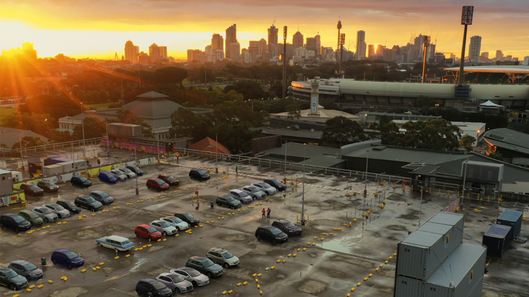 An aerial view of a rooftop drive-in cinema with the Sydney skyline in background at sunset