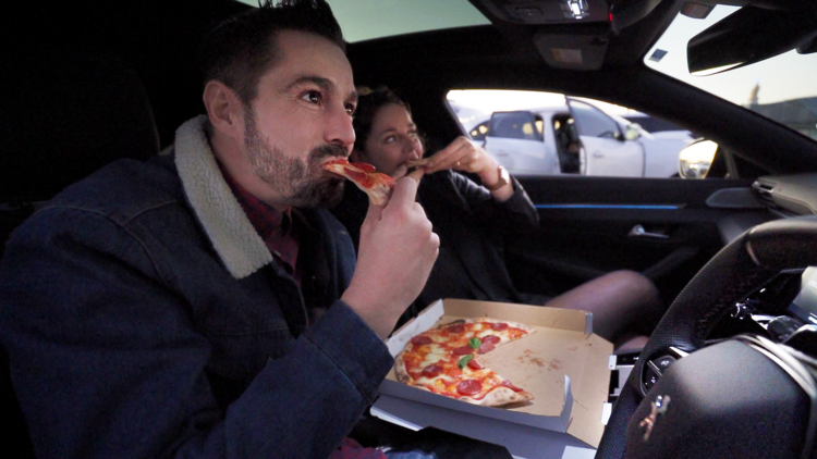 A couple is sitting in their car eating pizza and watching a movie