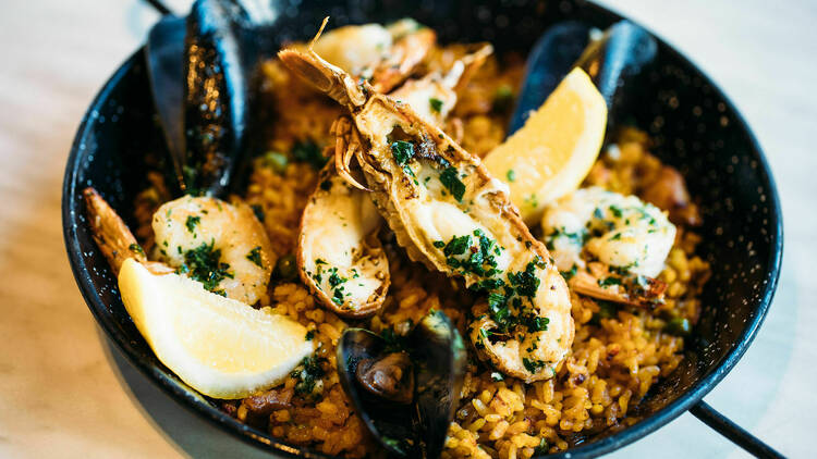 A black paella pan loaded with halved prawns, black mussels, lemon wedges and rice 