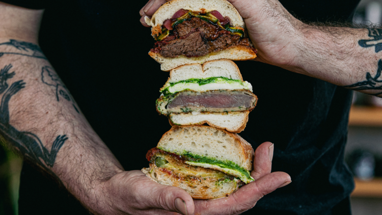 A man holding three halved sandwiche that have meat and schnitzel.