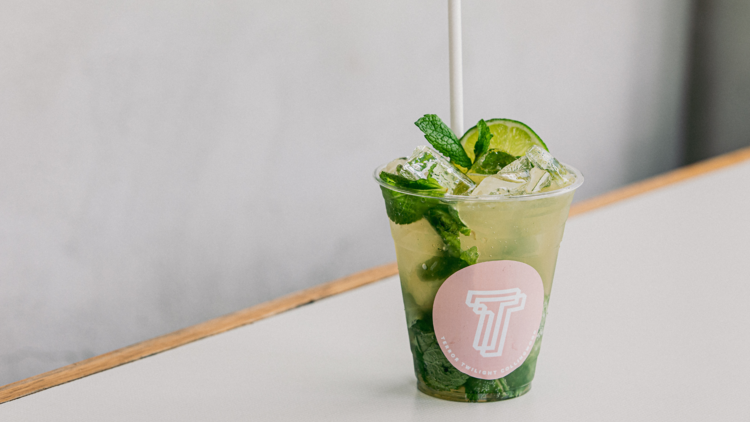 A mint julep cocktail in a plastic cup with mint leaves, a slice of lime and a paper straw.