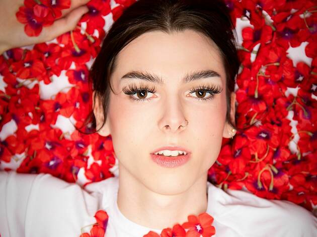 Three Winters Green, Fringe HQ 2021 a woman with dark hair wearing a white t shirt lies in a bed of red flower petals