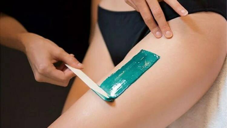 A woman applying a strip of hot wax to another woman's leg.