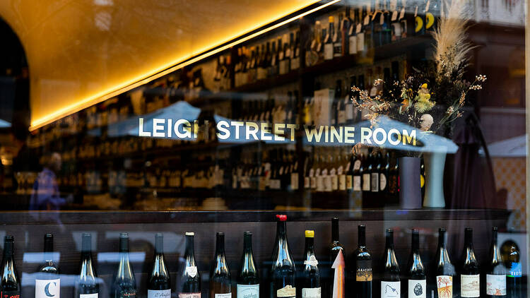 Looking through a restaurant window lined with bottles of wine. 'Leigh Street Wine Room' is printed on the window in gold