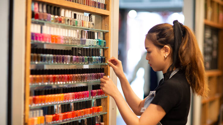 A nail salon employee grabbing nail polish off of a shelf.