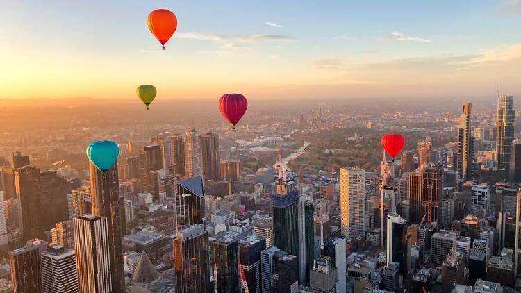 Five hot air balloons soar high above the city of Melbourne at sunrise